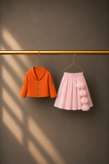 Anaario Orange Flamingo Jacket-Lehenga Set, orange jacket and blush pink lehenga on hangers