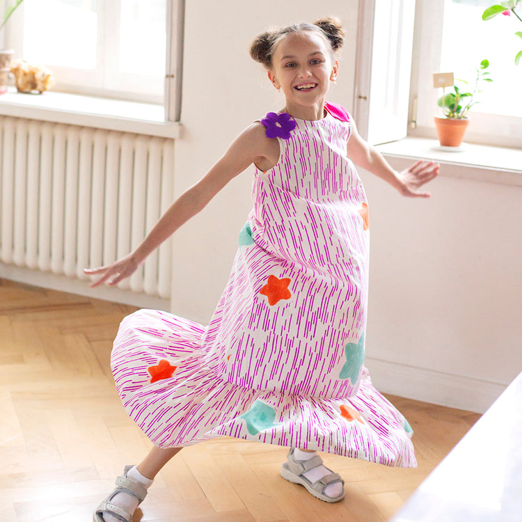 Girl wearing Anaario Sail Away maxi dress in white with pink dashed line print and colorful star appliques
