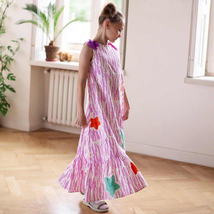 Girl wearing Anaario Sail Away maxi dress in white with pink dashed line print and colorful star appliques